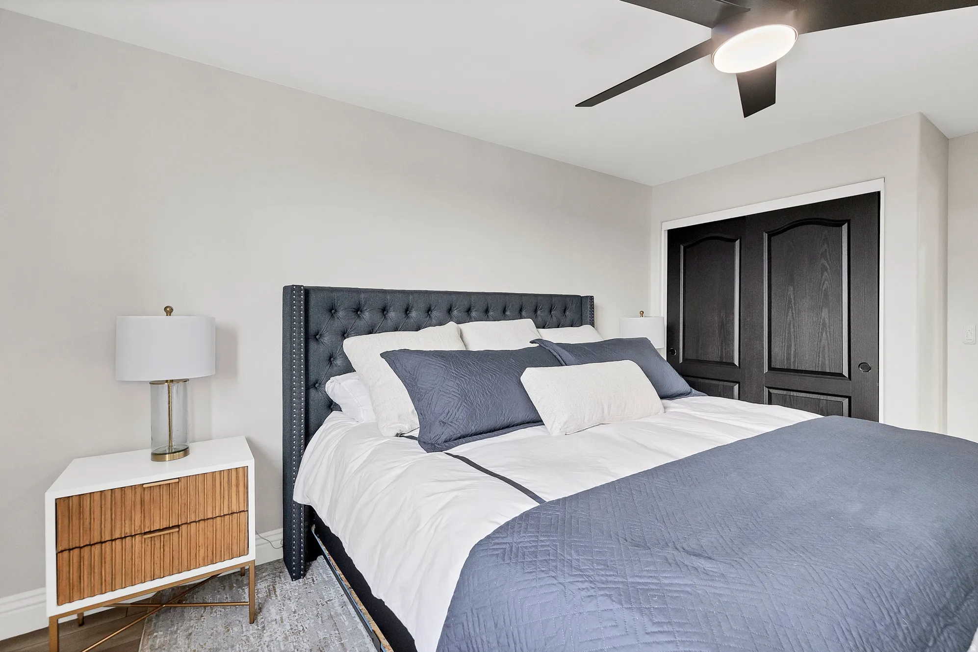 Bedroom featuring a tufted upholstered headboard, a ceiling fan with integrated lighting, and dark paneled bifold closet doors