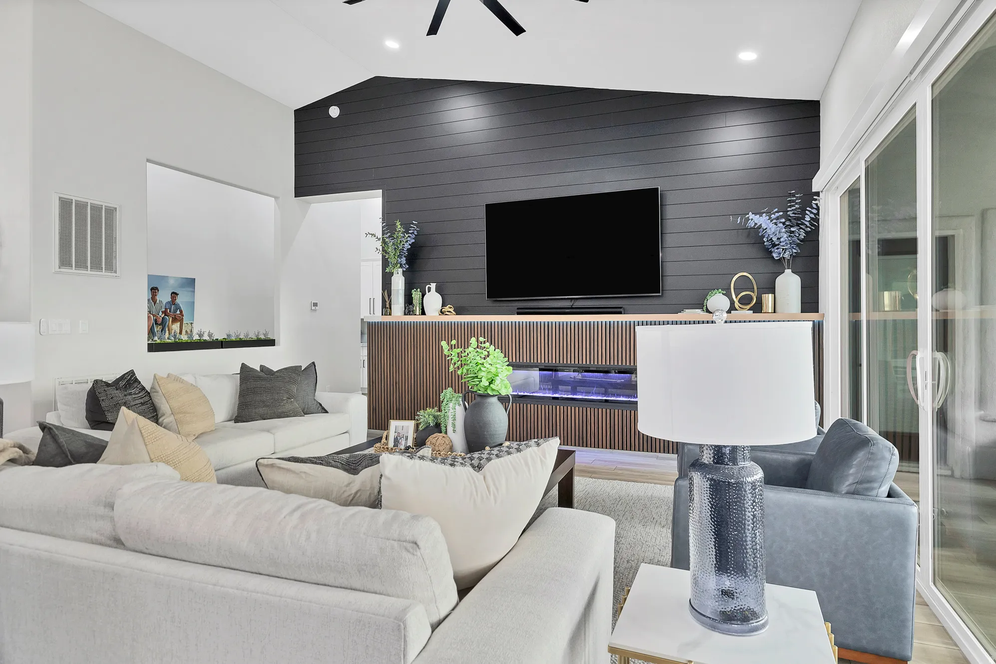 Vaulted ceiling living area featuring a dark shiplap accent wall, built-in media console with wood-finish paneling, recessed lighting, and sliding glass doors
