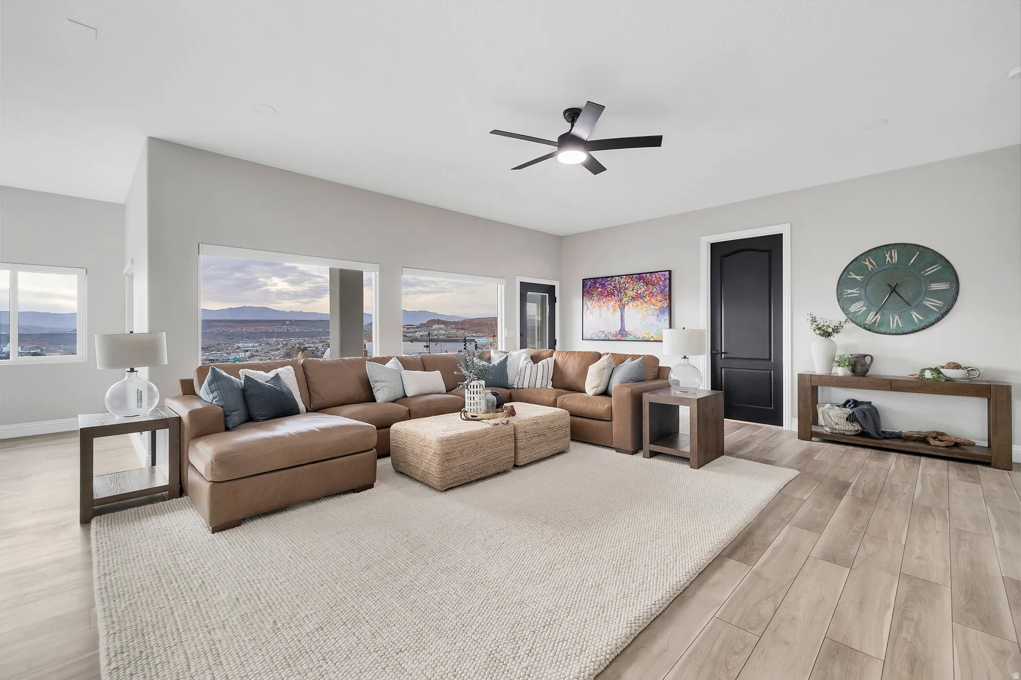 Spacious living area featuring large windows, wood-finish flooring, a contemporary ceiling fan, and light gray walls