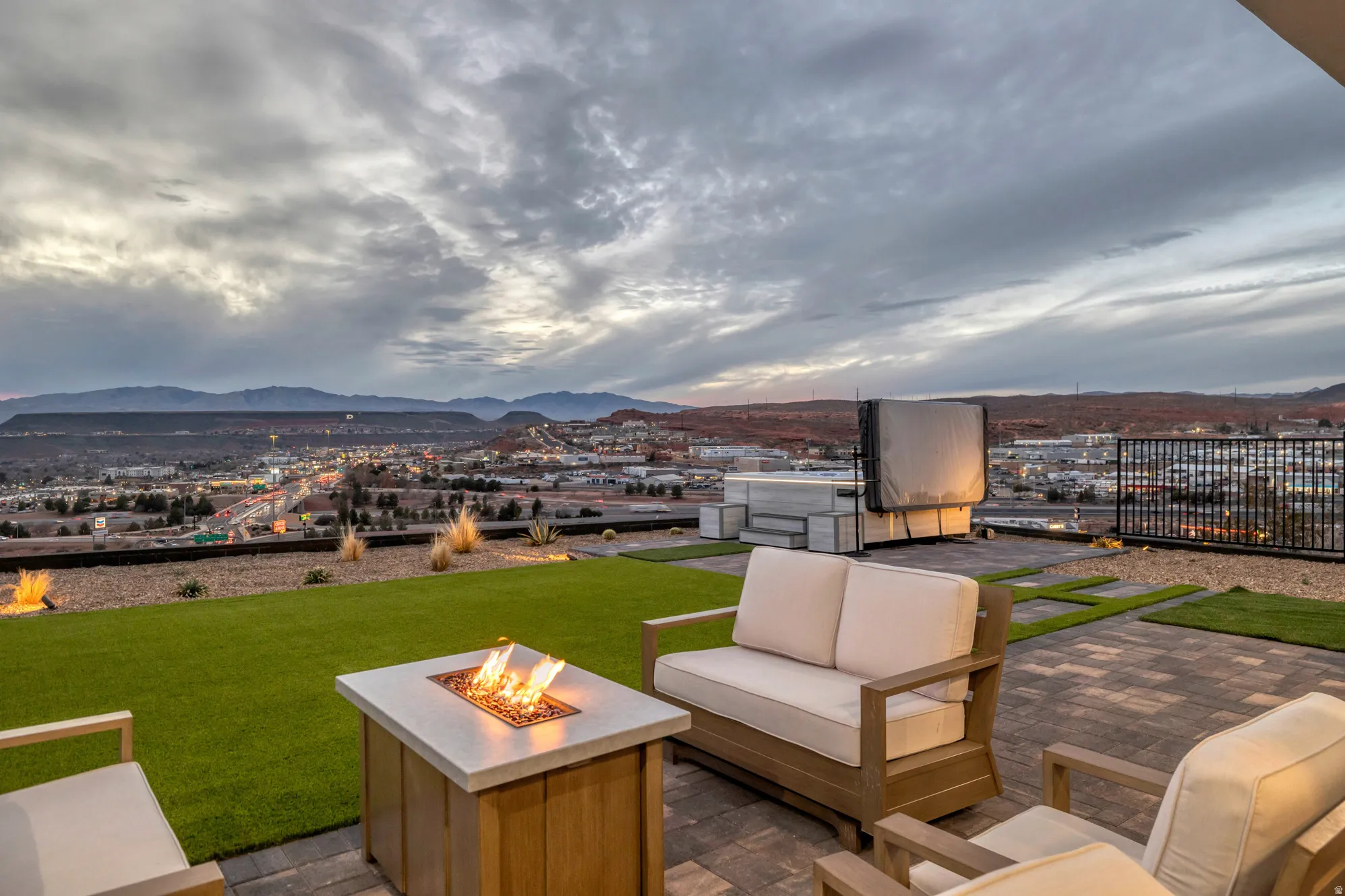 Outdoor patio featuring paver flooring, a built-in fire pit, artificial turf, low-maintenance landscaping, and surrounding mountain scenery