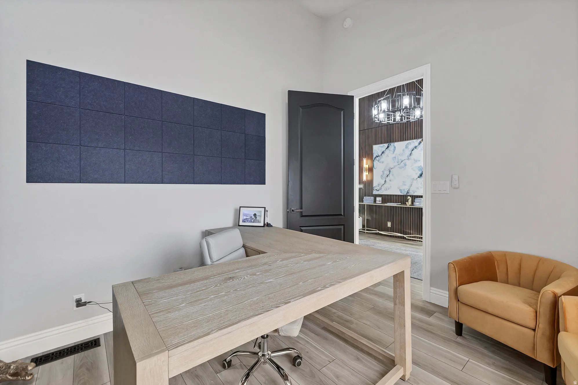 Spacious office area featuring light wood-finish flooring, a contemporary dark accent door, and a built-in wall panel accent
