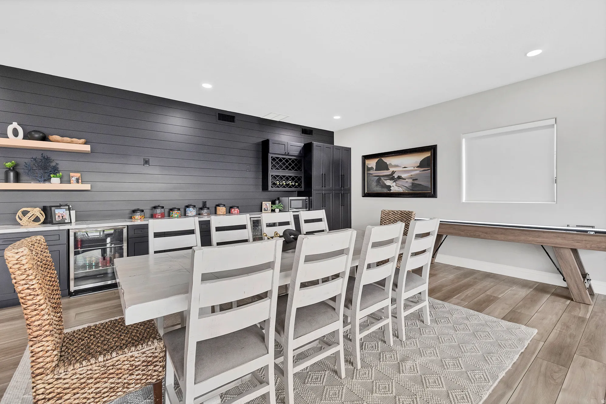 Spacious entertainment area featuring wood-finish flooring, a contemporary dining table with seating, and a shuffleboard table