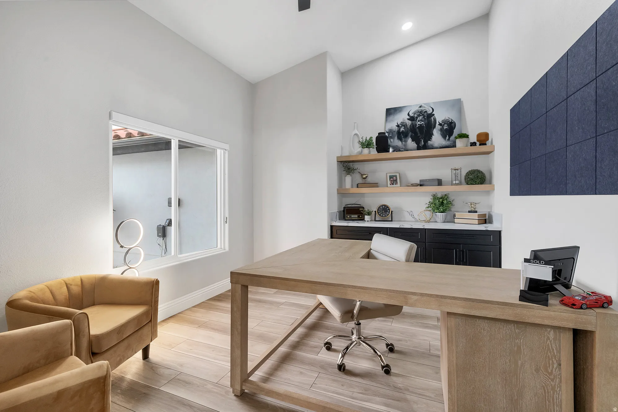 Office space featuring wood-finish flooring, a contemporary built-in desk, and a window with a white frame