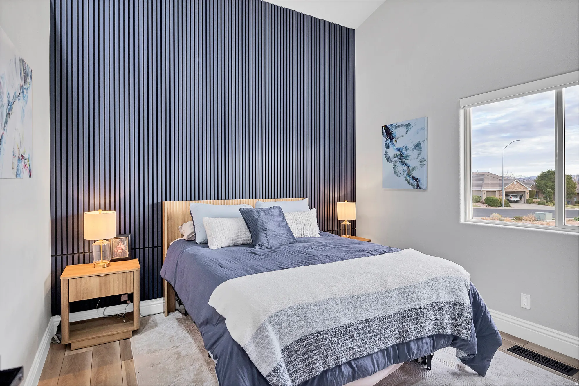 Accent wall with vertical paneling, vaulted ceiling, wood-finish flooring, ample natural light, and a large window