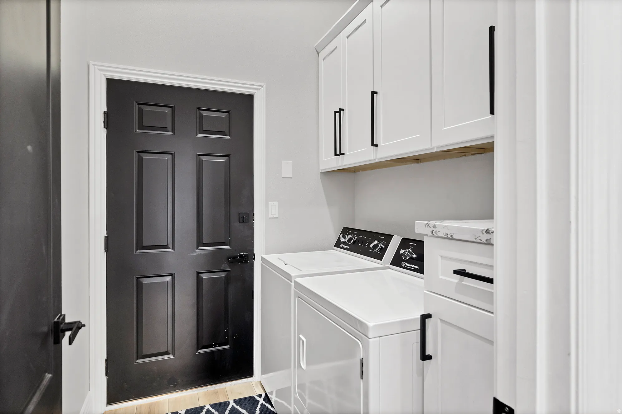 Dedicated laundry area featuring white shaker-style cabinetry with matte black hardware, a wood-finish shelf, and a built-in countertop