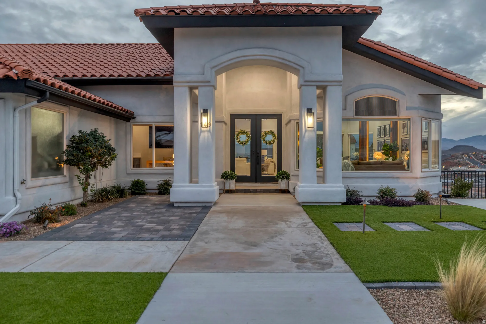Stucco exterior featuring a prominent arched entry, double glass-paneled front doors, red tile roofing, and an artificial turf lawn with integrated stepping stones
