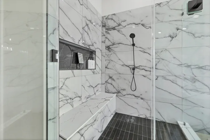 Walk-in shower featuring large format marble-look tile walls, a built-in shower bench, a recessed niche, dark tile flooring, and a matte black shower fixture