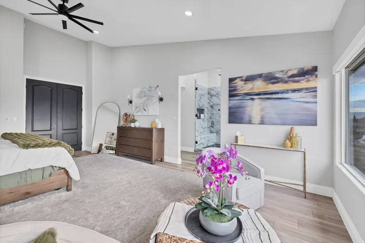 Spacious sleeping area featuring vaulted ceilings, a modern black ceiling fan, light-toned wood-finish flooring, and large windows