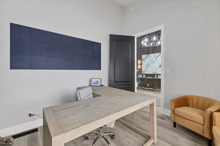 Spacious office area featuring light wood-finish flooring, a contemporary dark accent door, and a built-in wall panel accent