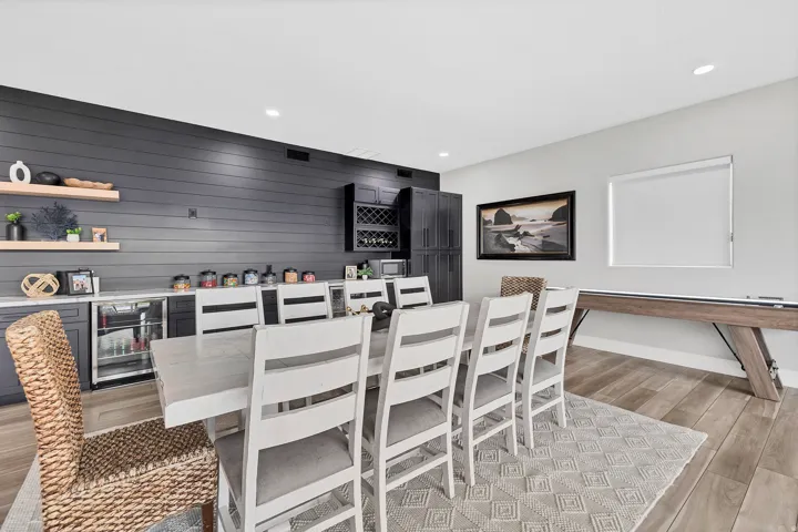 Spacious entertainment area featuring wood-finish flooring, a contemporary dining table with seating, and a shuffleboard table