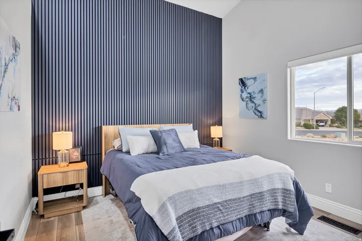 Accent wall with vertical paneling, vaulted ceiling, wood-finish flooring, ample natural light, and a large window