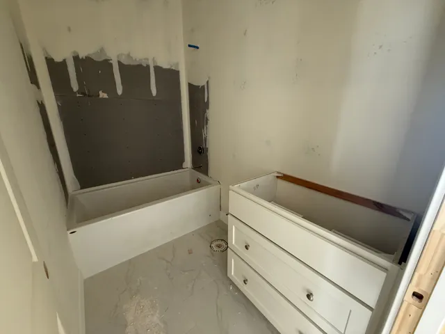 White bathtub installation, vanity cabinet with drawer storage, and light-toned tile flooring