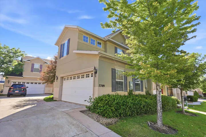 Multi-story stucco exterior featuring a two-car garage, dark window shutters, and multiple windows