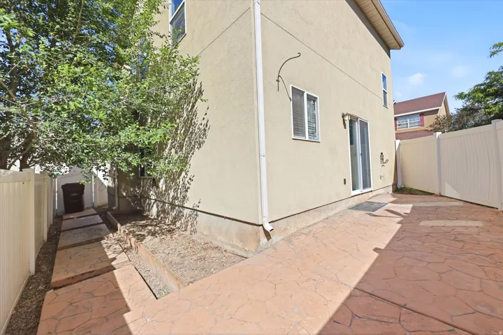 Stucco exterior featuring a stamped concrete patio, sliding glass door access, and a durable vinyl privacy fence
