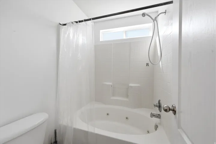 Soaking tub with integrated jets, white tile surround, and an overhead transom window