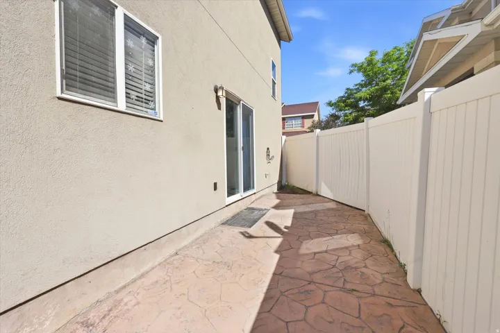Stamped concrete patio with a stucco exterior, sliding glass door, and a white privacy fence