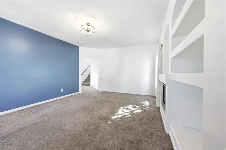 Carpeted living area featuring a blue accent wall, white walls, built-in shelving, an integrated fireplace, and an arched doorway