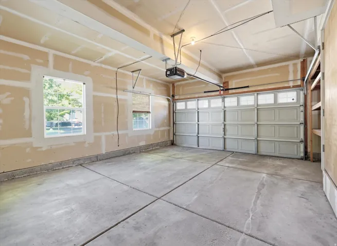 Spacious garage featuring a paneled overhead door with upper window inserts, two double-hung windows, concrete flooring, and built-in shelving