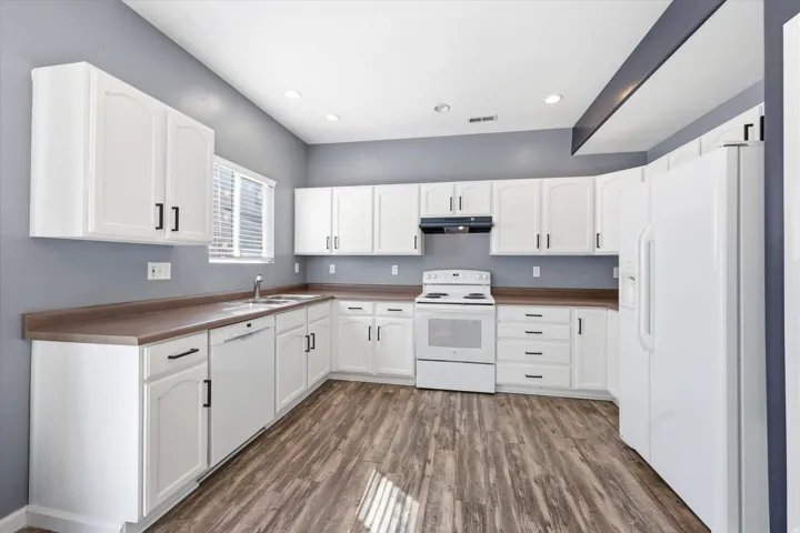 Spacious kitchen featuring extensive white cabinetry, wood-finish flooring, white appliances, and a double basin sink