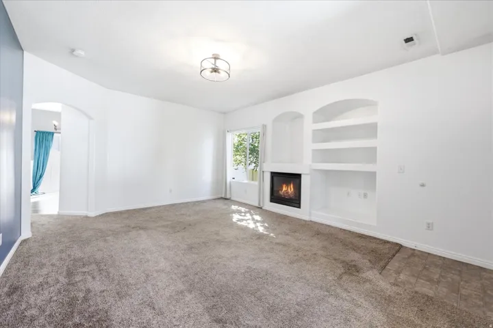 Living area featuring a built-in fireplace, integrated shelving, arched wall cutouts, light-toned carpeting, and a window with natural light