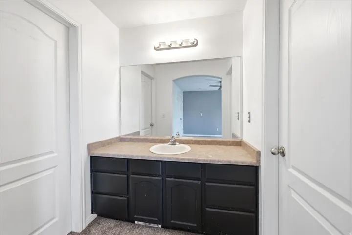 White vanity area featuring a single basin sink, laminate countertop, and black cabinetry