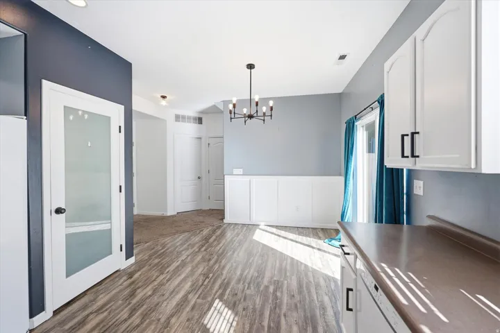 Open concept living space featuring wood-finish flooring, a contemporary chandelier, white wainscoting, and a glass-paneled interior door