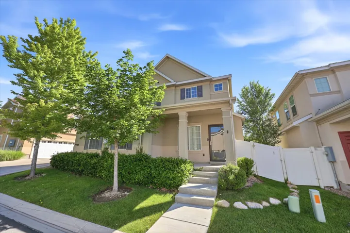 Multi-story stucco exterior featuring a covered porch with pillars, an entryway door with glass paneling, and upper-level windows with dark shutters