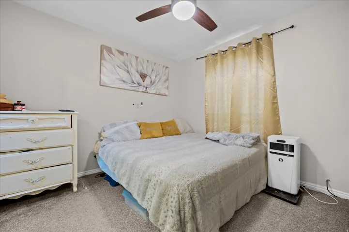 Bedroom featuring neutral wall paint, gray carpet, a ceiling fan with light fixture, and a window with curtain rod