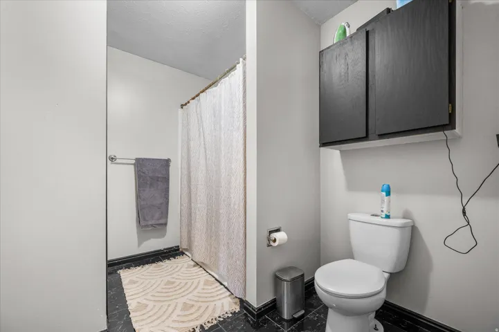 Bathroom featuring black tile flooring, white walls, and a white toilet