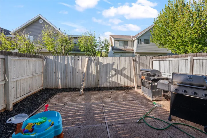 Paved patio area featuring a privacy fence, wood-chip landscaping, and a clear blue sky