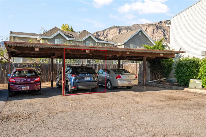 Covered parking space with marked designation, featuring a corrugated metal roof, wood support beams, and a gravel parking surface