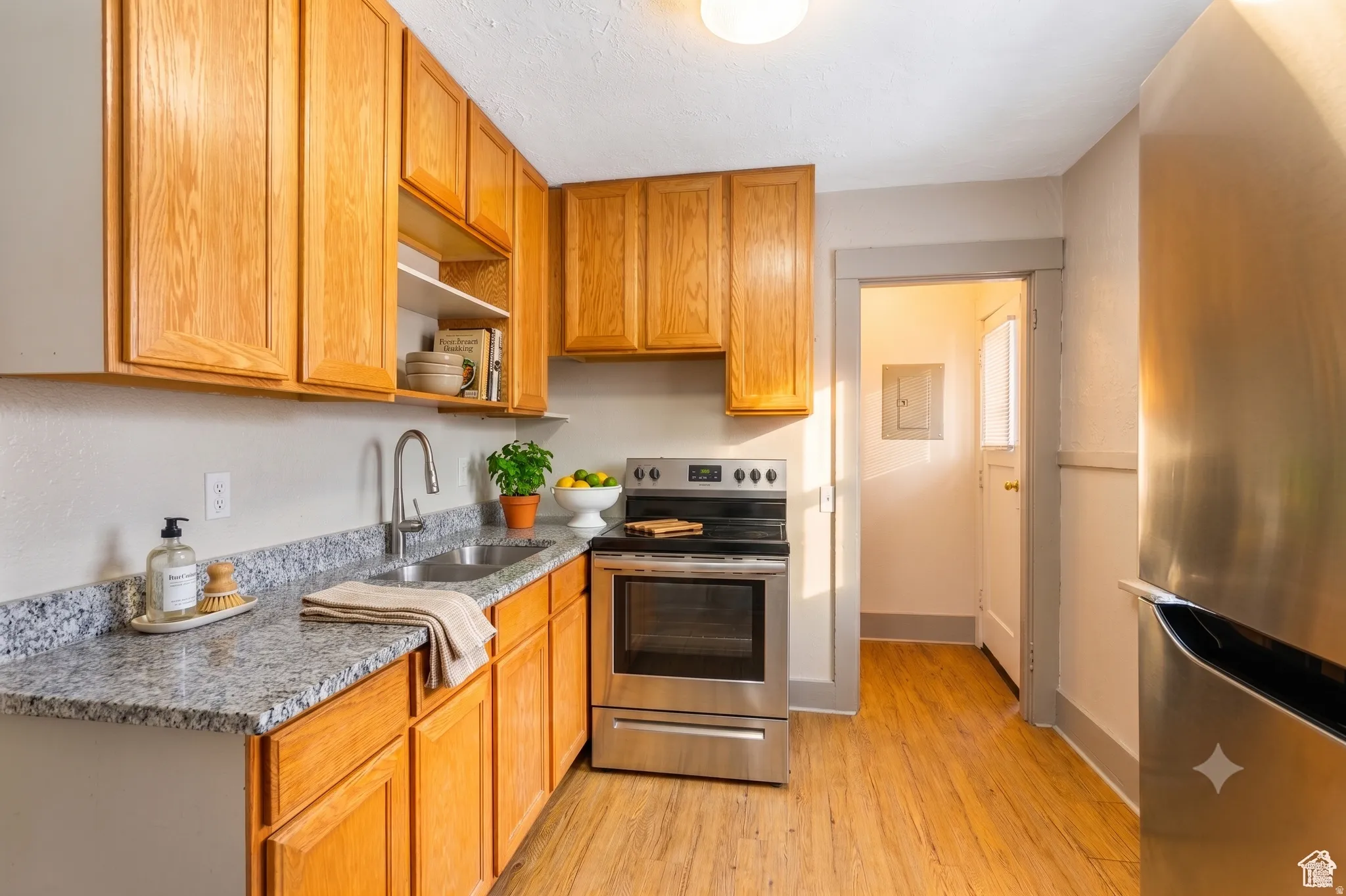Kitchen featuring wood-finish flooring, granite-style countertops, wood cabinetry, a stainless steel range, and a stainless steel refrigerator