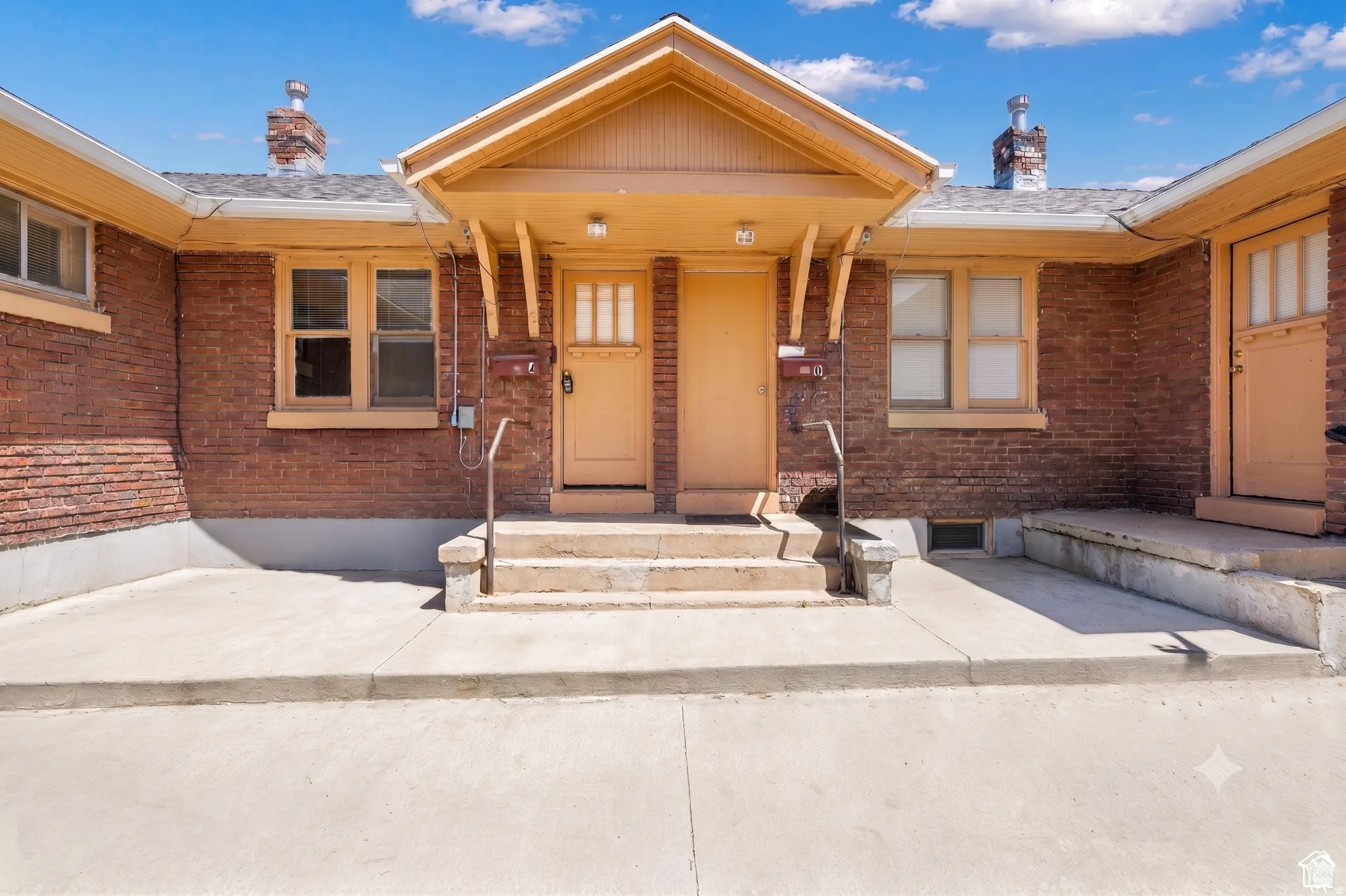 Brick exterior featuring a central covered entry, multiple individual entrances, and a concrete patio