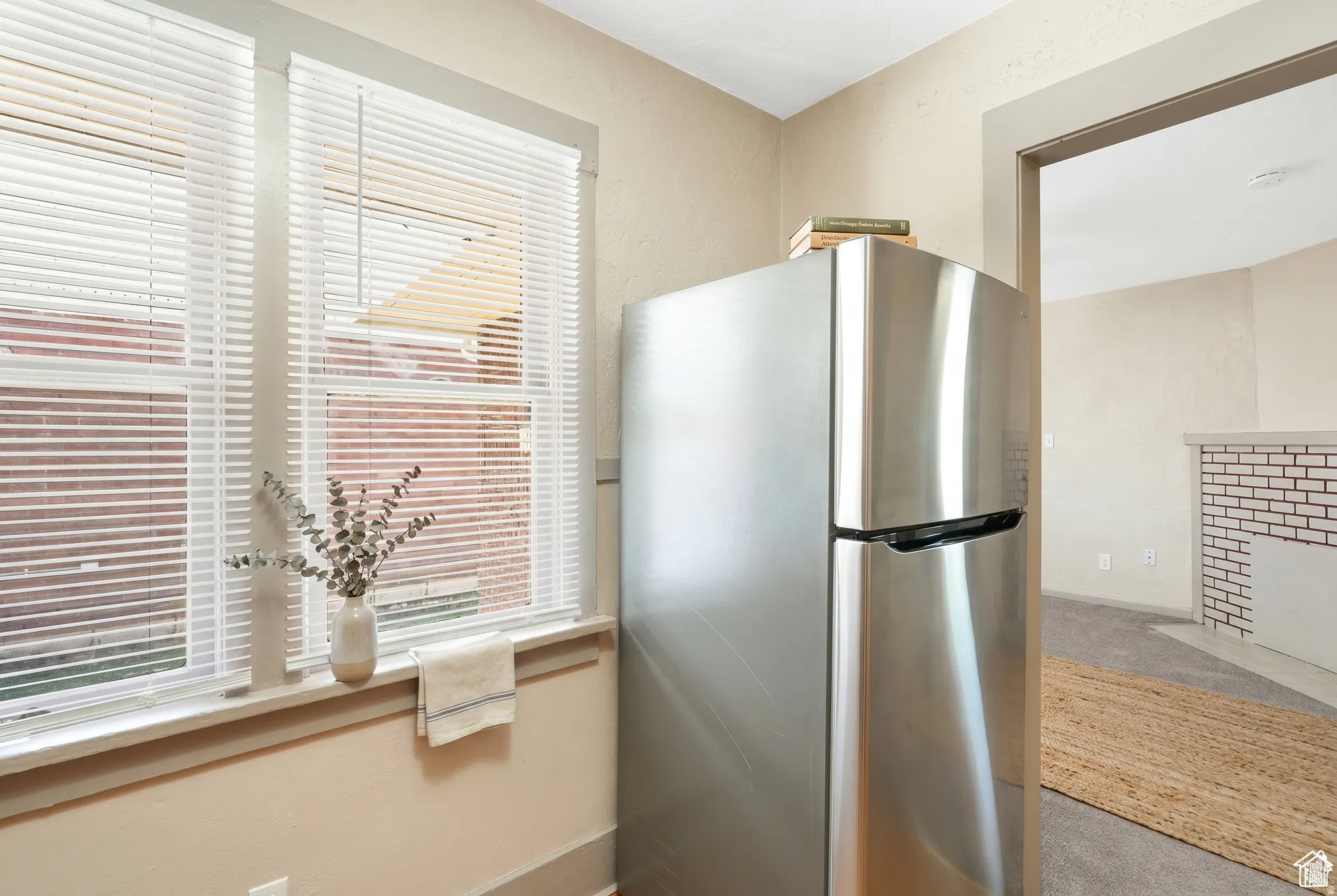 Stainless steel refrigerator with a top freezer, double-hung windows with blinds, and light-toned walls
