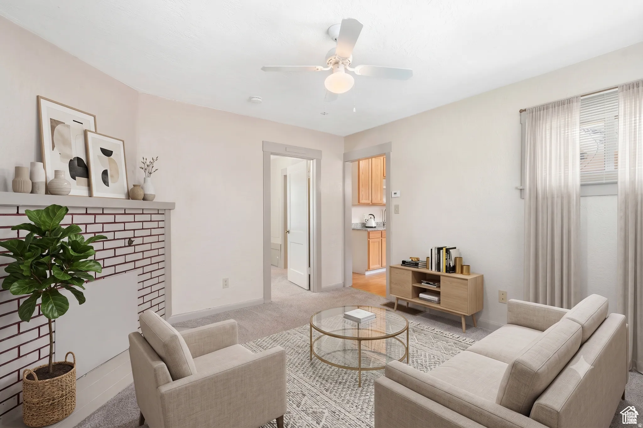 Living area featuring a white brick fireplace with a mantel, light-toned carpeting, and a ceiling fan with integrated lighting