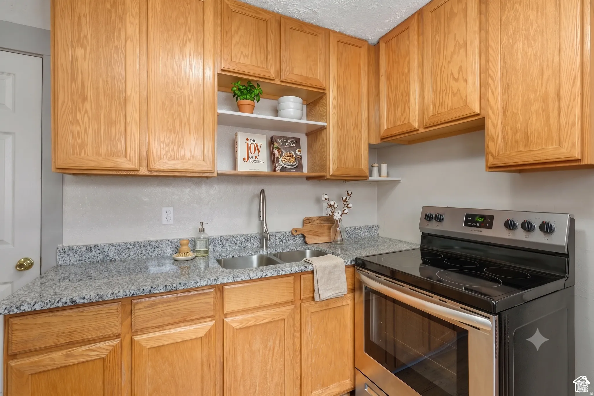 Kitchen featuring natural wood cabinetry, light-toned countertops, a stainless steel electric range, and a double-basin sink with a gooseneck faucet
