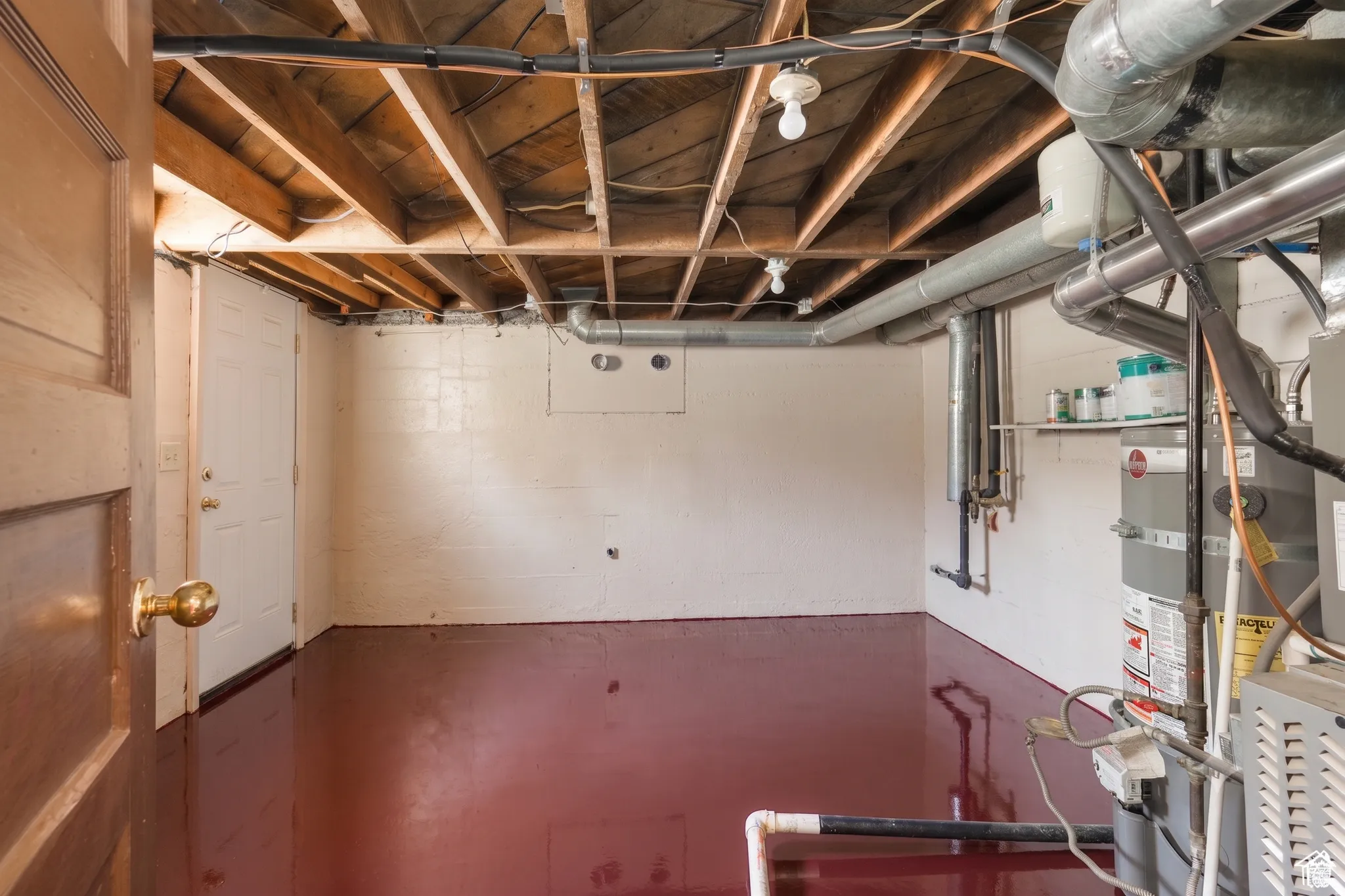 Finished basement space featuring exposed wood joists and an industrial red-painted concrete floor