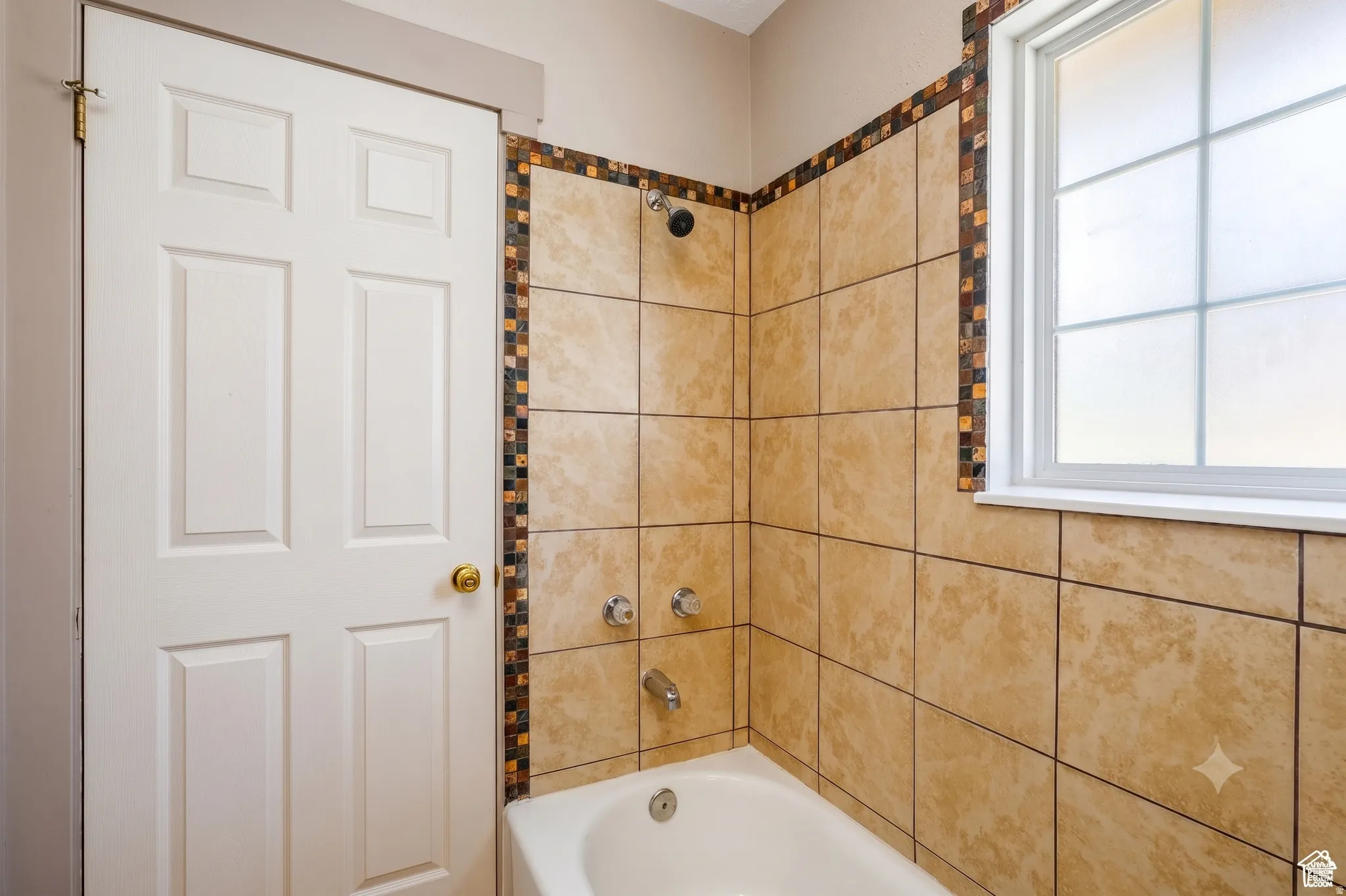 Bathtub with a tiled surround featuring decorative mosaic accents