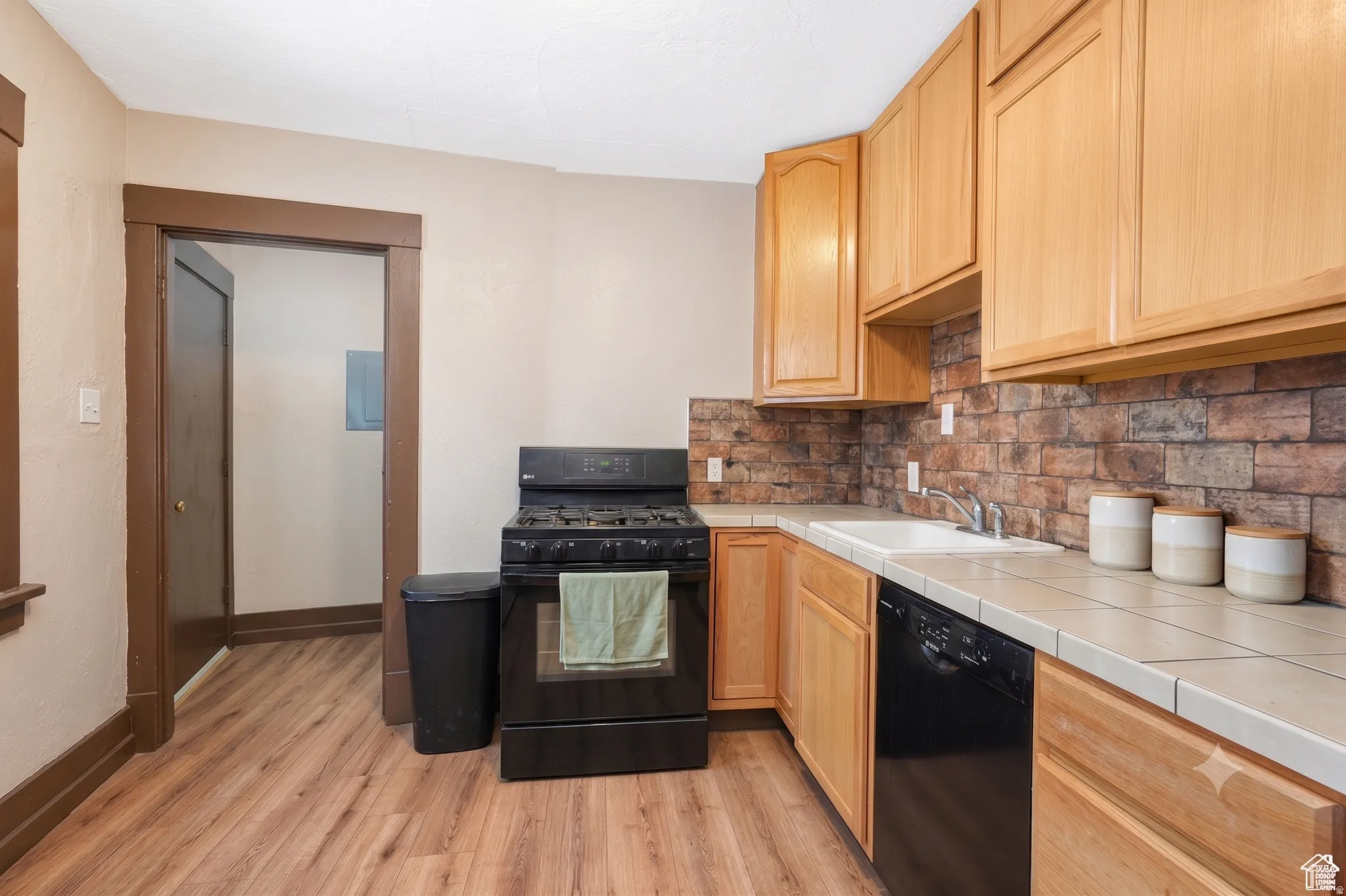Kitchen featuring wood-finish flooring, light wood cabinetry, a tile countertop, and a brick-look tile backsplash