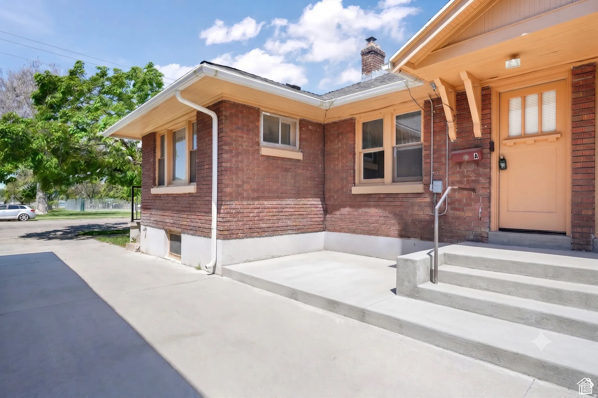 Brick exterior with a prominent entry porch, featuring a wooden door with transom lites, concrete steps, and a metal handrail