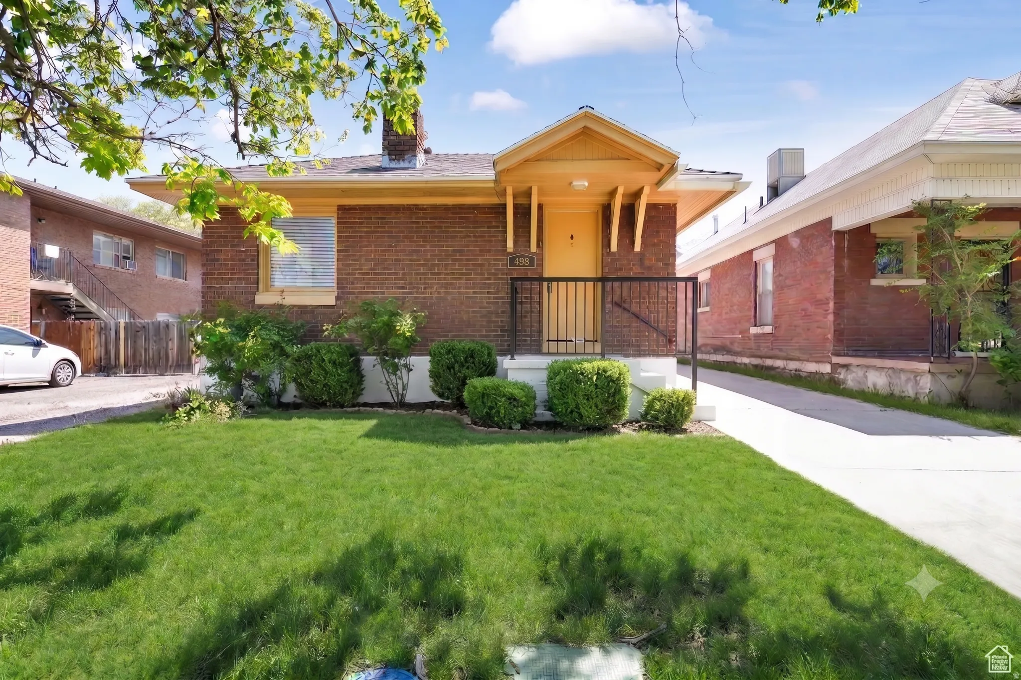 Brick exterior with a prominent yellow entry porch, black metal handrails, and mature front landscaping