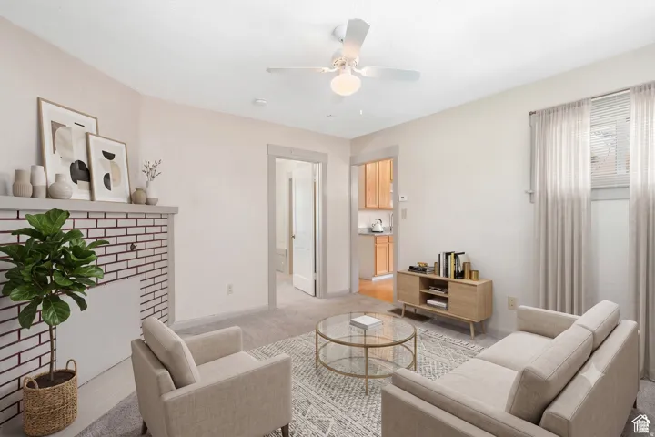 Living area featuring a white brick fireplace with a mantel, light-toned carpeting, and a ceiling fan with integrated lighting