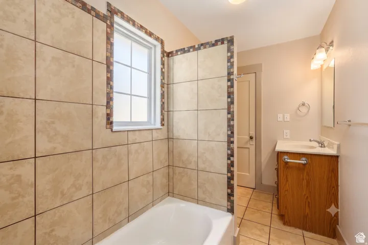 Bathroom featuring a tub with large format tile surround, decorative mosaic tile accents, and a window