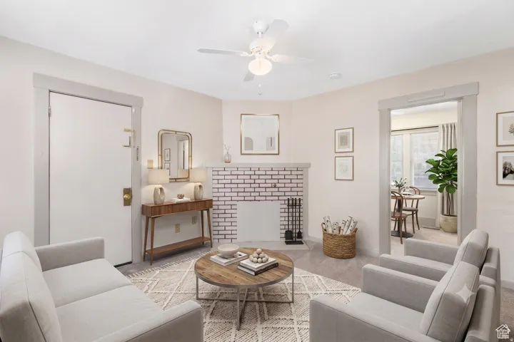 Living space featuring light-toned wall finishes, carpet flooring, a ceiling fan, and an exposed brick fireplace