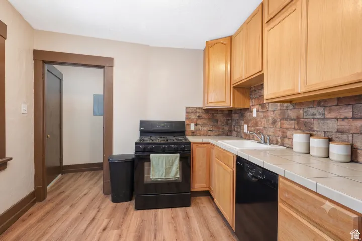 Kitchen featuring wood-finish flooring, light wood cabinetry, a tile countertop, and a brick-look tile backsplash