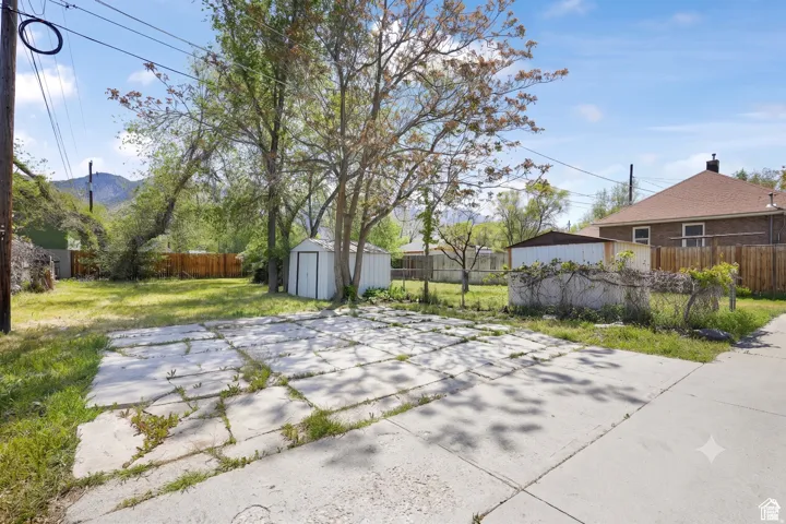 Expansive backyard featuring a concrete patio, mature trees, a storage shed, and partial fencing