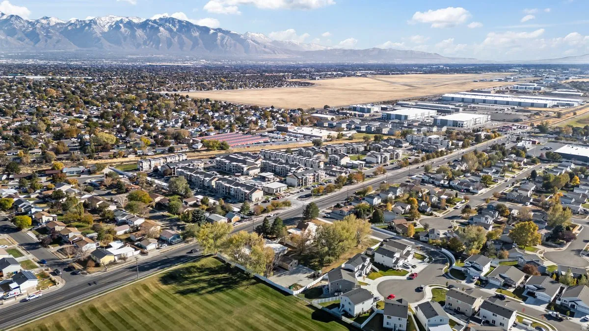 Expansive aerial perspective showcasing a residential community with varied architectural styles, a large green space, and distant mountain ranges
