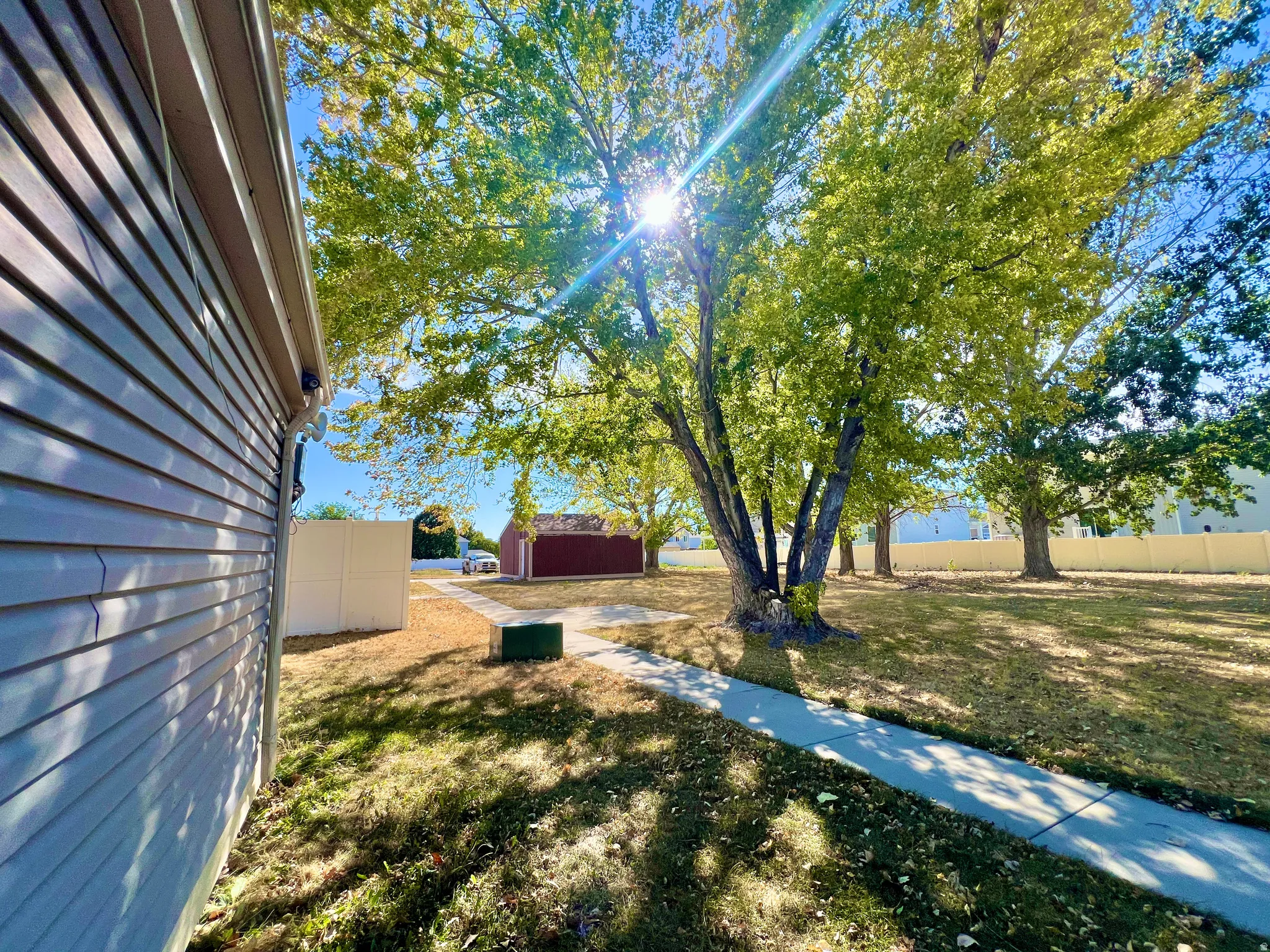 Expansive side yard featuring mature trees, a concrete pathway, and a vinyl-sided building with gutters
