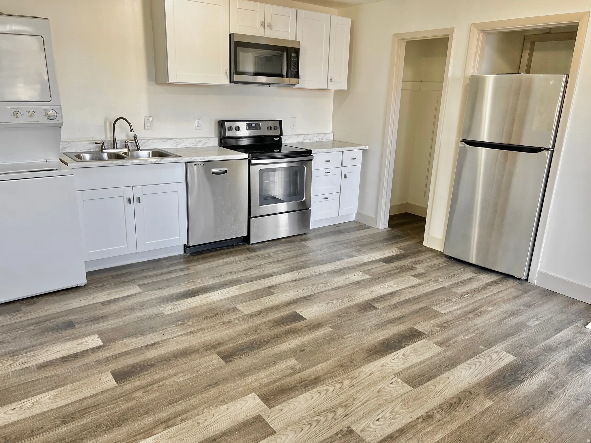 Kitchen featuring wood-finish flooring, white cabinetry, stainless steel appliances, and a stackable washer and dryer unit