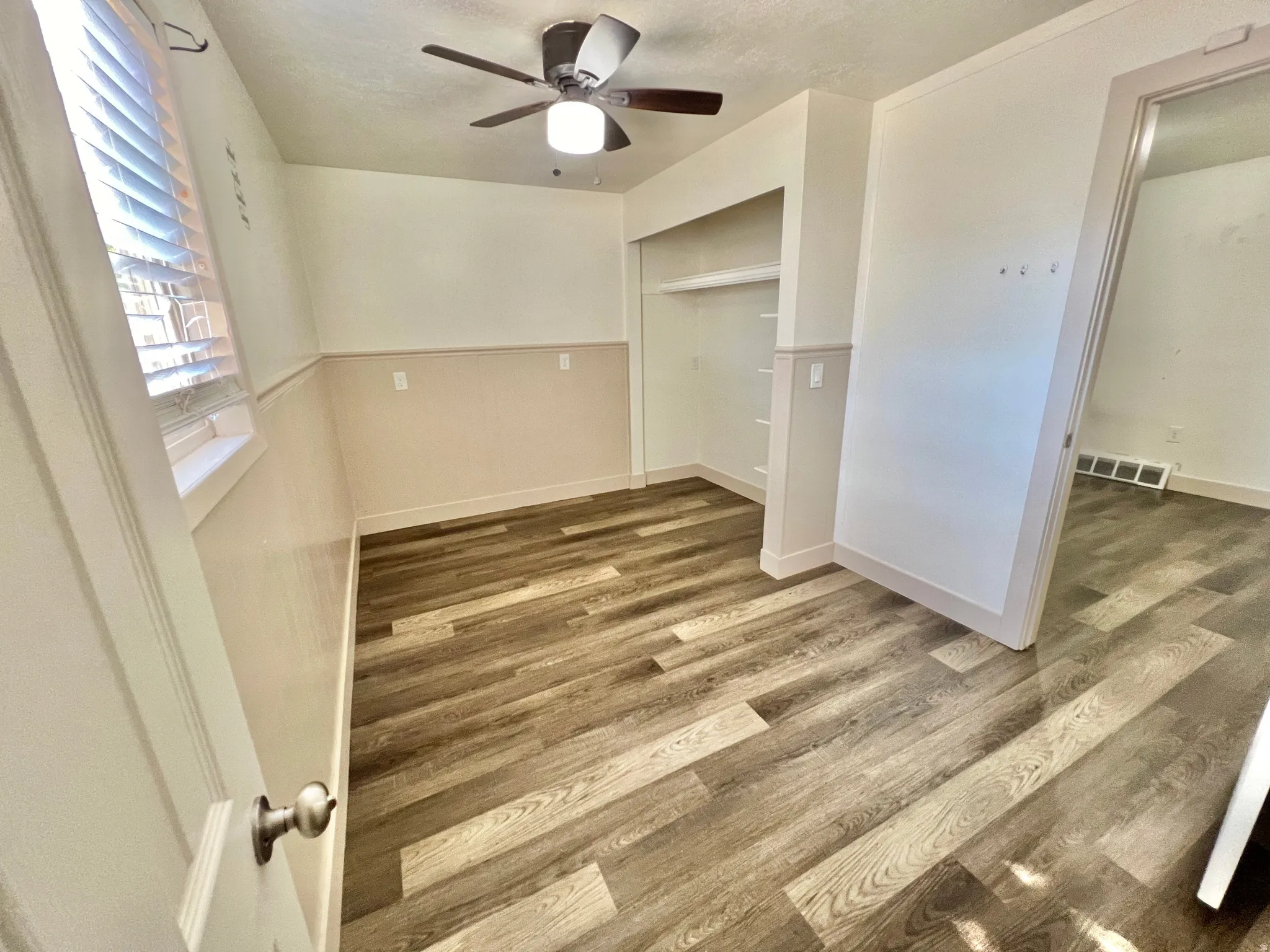 Interior room featuring wood-finish flooring, a built-in closet with shelving, and a ceiling fan with integrated lighting